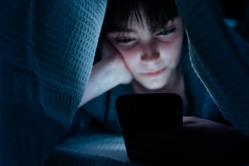 Teenager-Mädchen, das ein Smartphone benutzt und sich nachts unter einer Decke versteckt, in sozialen Netzwerken unterwegs. - HPIF05788