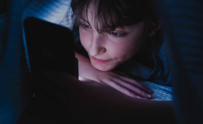 A happy teen girl using smartphone, hiding under blanket at nigh, social networks cocnept. - HPIF05789