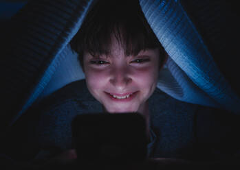 A happy teen girl using smartphone, hiding under blanket at nigh, social networks cocnept. - HPIF05791