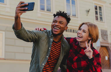 Junges gemischtrassiges Paar macht Selfie für soziale Netzwerke im Freien in einer Stadt. - HPIF05795