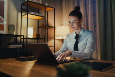 A happy mid adult business woman with diary working on laptop in office at night. - HPIF05838