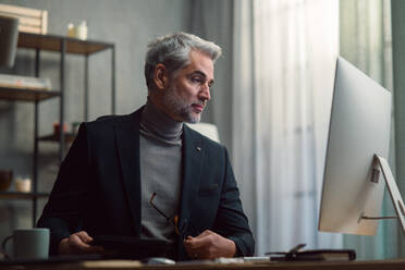 A mature businessman working on computer indoors in office. - HPIF05847