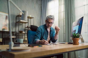 A mature man architect working on computer at desk indoors in office. - HPIF05863