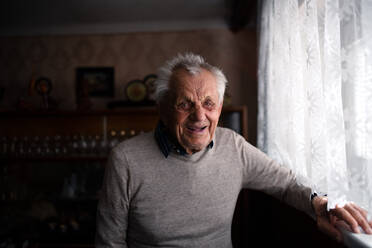 A portrait of elderly man standing indoors at home, looking at camera and laughing. - HPIF05868