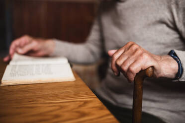 An unrecognizable elderly man sitting at the table indoors at home, reading book. - HPIF05873