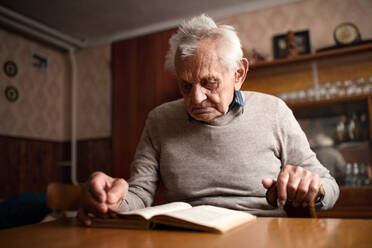 Ein Porträt eines älteren Mannes, der zu Hause am Tisch sitzt und ein Buch liest. - HPIF05874