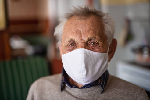 Porträt eines älteren Mannes mit Gesichtsmaske, der zu Hause in die Kamera schaut, Konzept des Coronavirus. - HPIF05876