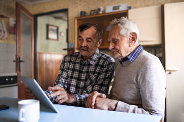A portrait of man with elderly father sitting at the table indoors at home, using tablet. - HPIF05879