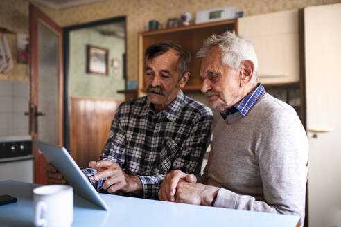 Ein Porträt eines Mannes mit einem älteren Vater, der zu Hause am Tisch sitzt und ein Tablet benutzt. - HPIF05879