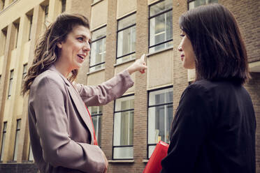 Geschäftsfrau gestikuliert und spricht mit einem Kollegen vor einem Gebäude - PWF00556