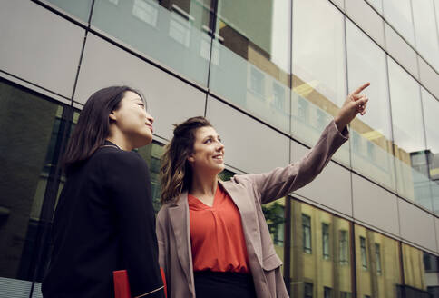 Happy businesswoman gesturing and standing with colleague in front of building - PWF00557