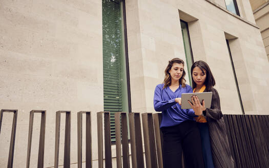 Businesswoman with colleague using tablet PC standing in front of building - PWF00584