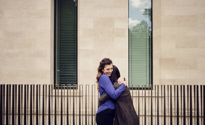 Happy businesswoman hugging colleague standing in front of building - PWF00585