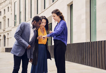 Businessman and businesswomen checking time standing in front of building - PWF00592