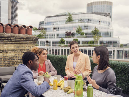 Businesswoman talking to colleagues and having lunch together at table - PWF00603