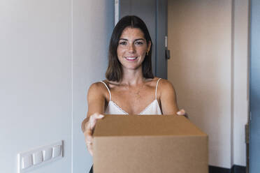 Happy woman holding box container at home - PNAF04828