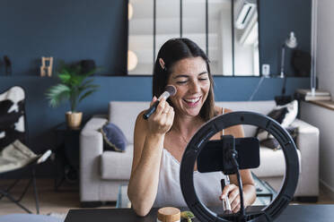 Happy influencer recording make-up tutorial on smart phone at home - PNAF04831