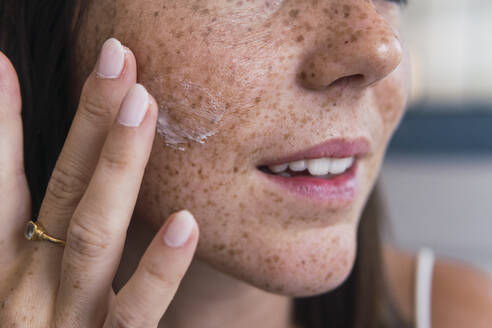 Hand einer Frau, die Feuchtigkeitscreme auf das Gesicht aufträgt - PNAF04843