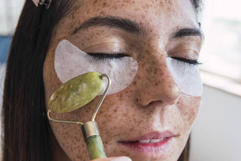 Woman with freckle face massaging using jade stone roller - PNAF04848