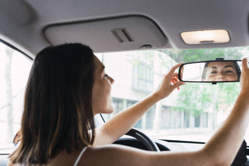 Young woman adjusting rear view mirror in car - PNAF04856