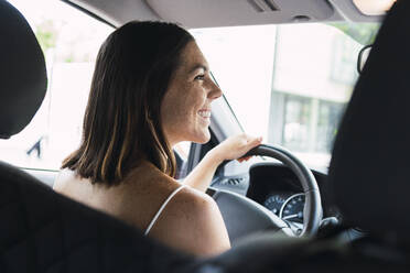 Happy young woman sitting on driver's seat in car - PNAF04857