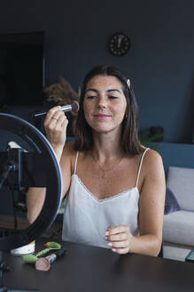 Lächelnde junge Frau, die zu Hause Make-up aufträgt und eine Anleitung auf ihrem Smartphone vloggt - PNAF04864