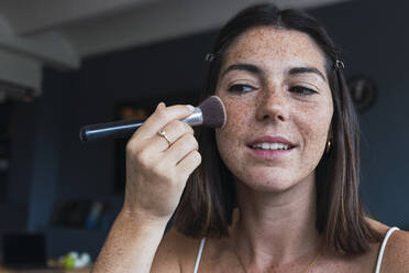 Woman with freckle face applying makeup at home - PNAF04865