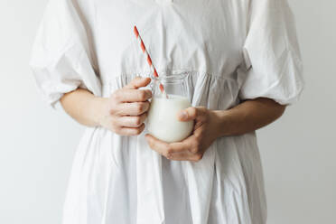Frau hält ein Glas Milchshake mit Strohhalm vor einer Wand - EGHF00698