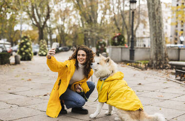 Glückliche junge Frau, die ein Selfie mit ihrem Hund über ihr Smartphone auf einem Fußweg macht - JCCMF08853
