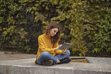 Young woman using tablet computer sitting on seat - JCCMF08911