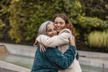 Happy young woman hugging grandmother in park - JCCMF08924