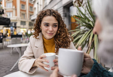 Lächelnde junge Frau mit Kaffeetasse und Großmutter in einem Straßencafé - JCCMF08927