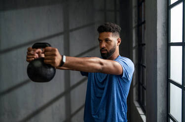 Ein junger afroamerikanischer Sportler steht und hebt eine Kesselglocke in der Halle, Workout-Trainingskonzept. - HPIF05916