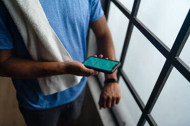 An unrecognizable young African American sportsman standing indoors at gym, using smartphone and smartwatch. - HPIF05920