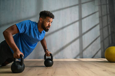 Ein junger afroamerikanischer Sportler macht Liegestütze mit Kettle Bells in einer Halle, Trainingskonzept. - HPIF05923