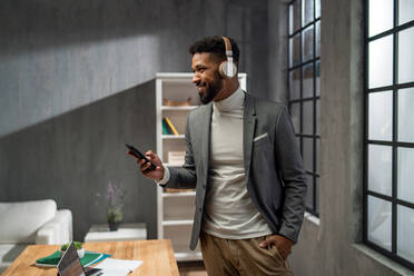 A happy young african american businessman with smartphone and headset working indoors in office - HPIF05932