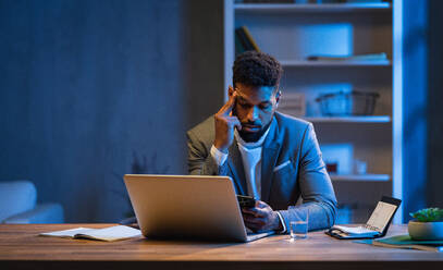 Ein junger afroamerikanischer Geschäftsmann arbeitet nachts in einem Büro. - HPIF05942
