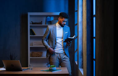 Ein junger afroamerikanischer Geschäftsmann, der nachts im Büro seinen Terminkalender betrachtet. - HPIF05947
