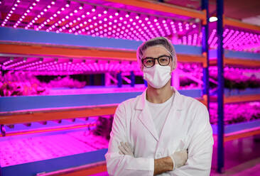 Front view of worker with face mask on aquaponic farm, sustainable business and coronavirus. - HPIF05978