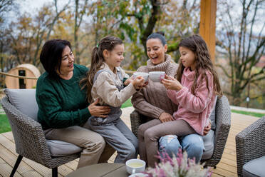 Two happy sisters with a mother and grandmother sitting and drinking tea outdoors in patio in autumn. - HPIF05993