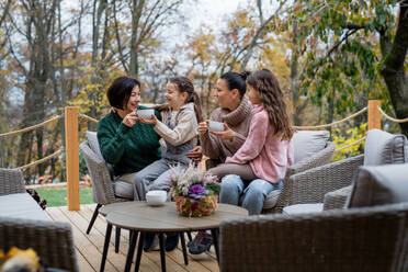 Zwei glückliche Schwestern mit einer Mutter und einer Großmutter, die im Herbst im Innenhof sitzen und Tee trinken. - HPIF05994