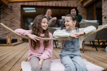 Two happy sisters with a mother and grandmother sitting outdoors in patio in autumn. - HPIF05995