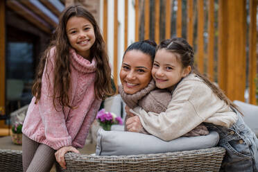 Two happy sisters with a mother embracing and looking at camera outdoors in patio in autumn. - HPIF05996