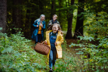 Ein glückliches kleines Mädchen mit Korb läuft während eines Spaziergangs mit Mutter und Großmutter im Freien im Wald - HPIF06008