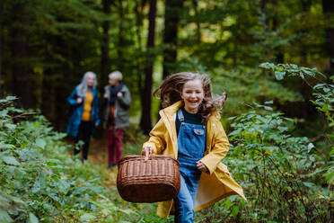 Ein glückliches kleines Mädchen mit Korb läuft während eines Spaziergangs mit Mutter und Großmutter im Freien im Wald - HPIF06009