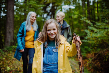 Ein glückliches kleines Mädchen mit Korb läuft während eines Spaziergangs mit Mutter und Großmutter im Freien im Wald - HPIF06011