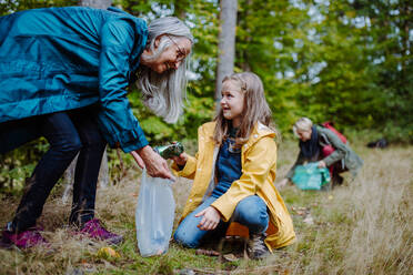 Ein kleines Mädchen mit Mutter und Großmutter beim Aufsammeln von Müll im Wald. - HPIF06024