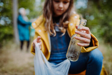 Nahaufnahme eines kleinen Mädchens, das draußen im Wald an einem Herbsttag Abfall in einer Plastiktüte aufsammelt. - HPIF06027