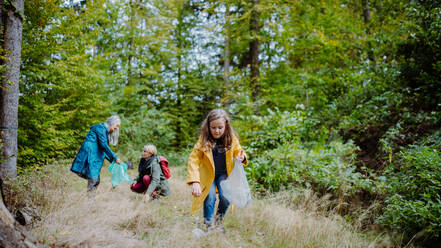 Ein kleines Mädchen mit Mutter und Großmutter beim Aufsammeln von Müll im Wald. - HPIF06028