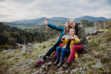 Ein kleines Mädchen mit Mutter und Großmutter, die ein Selfie auf dem Gipfel eines Berges machen. - HPIF06050